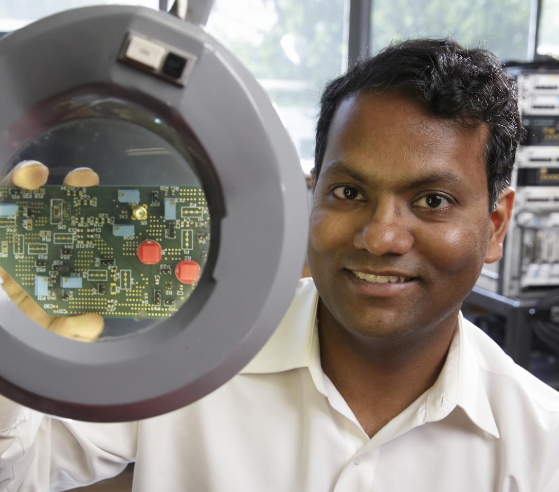 Photo of Sudip Shekhar holding a chip being viewed through a microscope