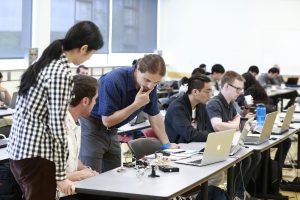 Lukas Chrostowski looking at a laptop with his students looking on