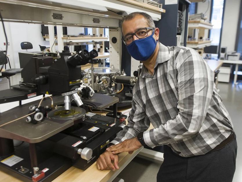 Behraad Bahreyni leaning on a counter in front of a microscope in a laboratory