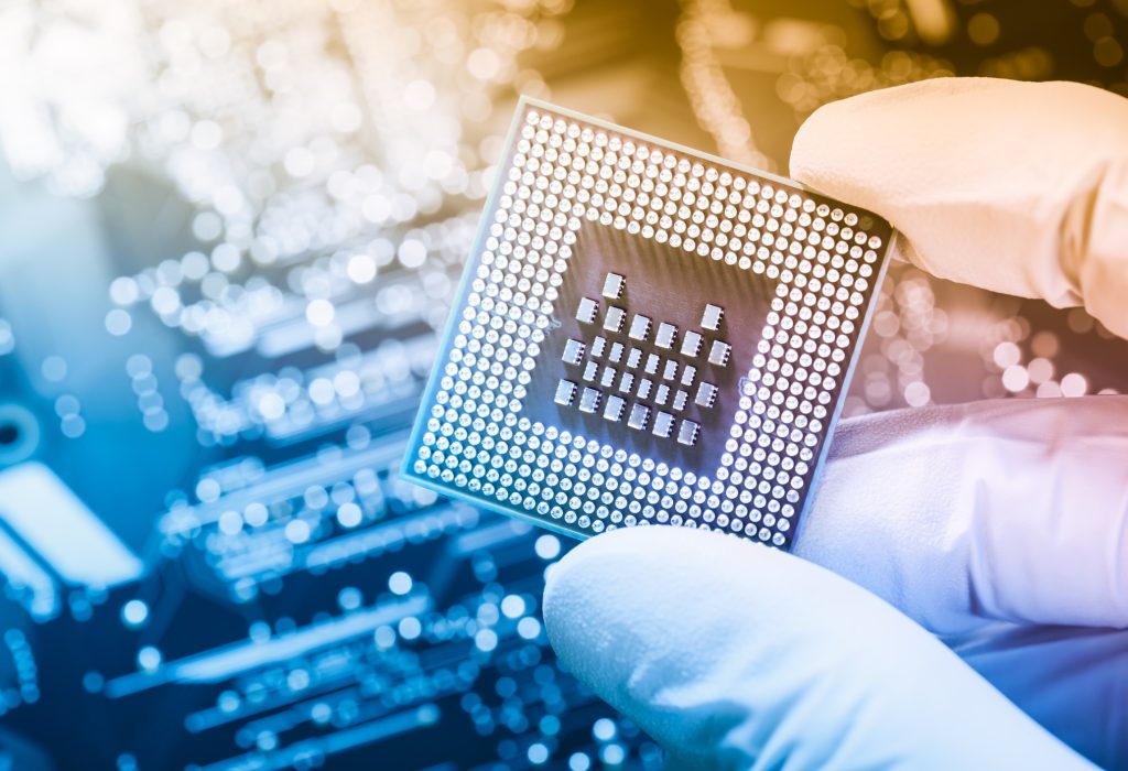 Electronic technician with glowes holding chip. Nice bokeh from circuit board in background. Warm light from top right corner.