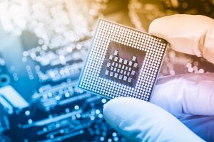 Close up of technician holding chip over defocused circuit board